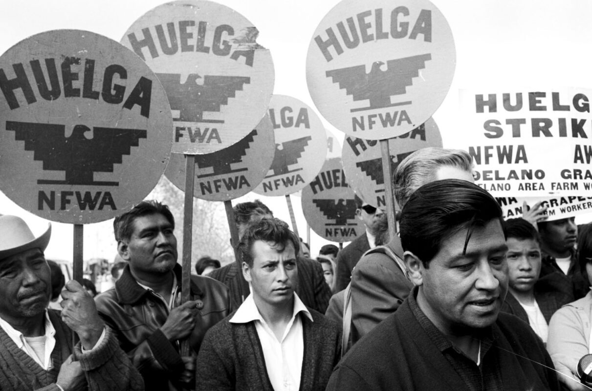 César Chávez walking with farmworkers carrying strike signs, Delano, CA, 1966.